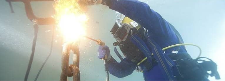 A diver welding underwater, the arc flaring in pale, hazy water