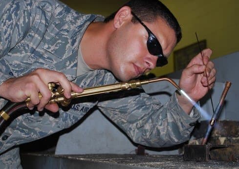 Torch brazing: an operator in shaded safety glasses heating a joint with an oxy-fuel torch and feeding a brazing rod