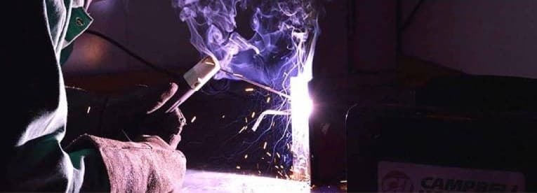 A gloved hand striking a stick electrode against steel, sparks scattering