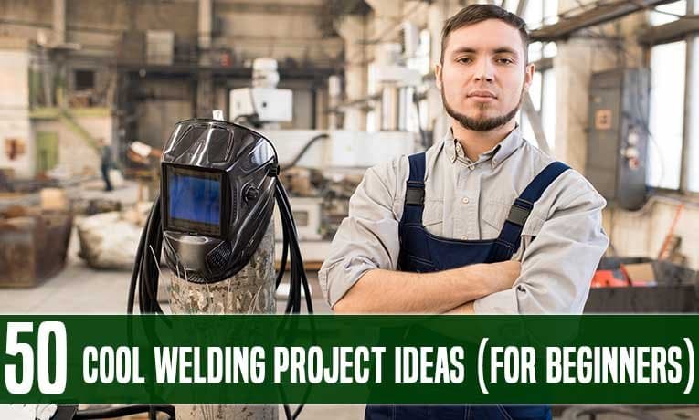 A welder standing with his arms crossed beside a helmet in a workshop