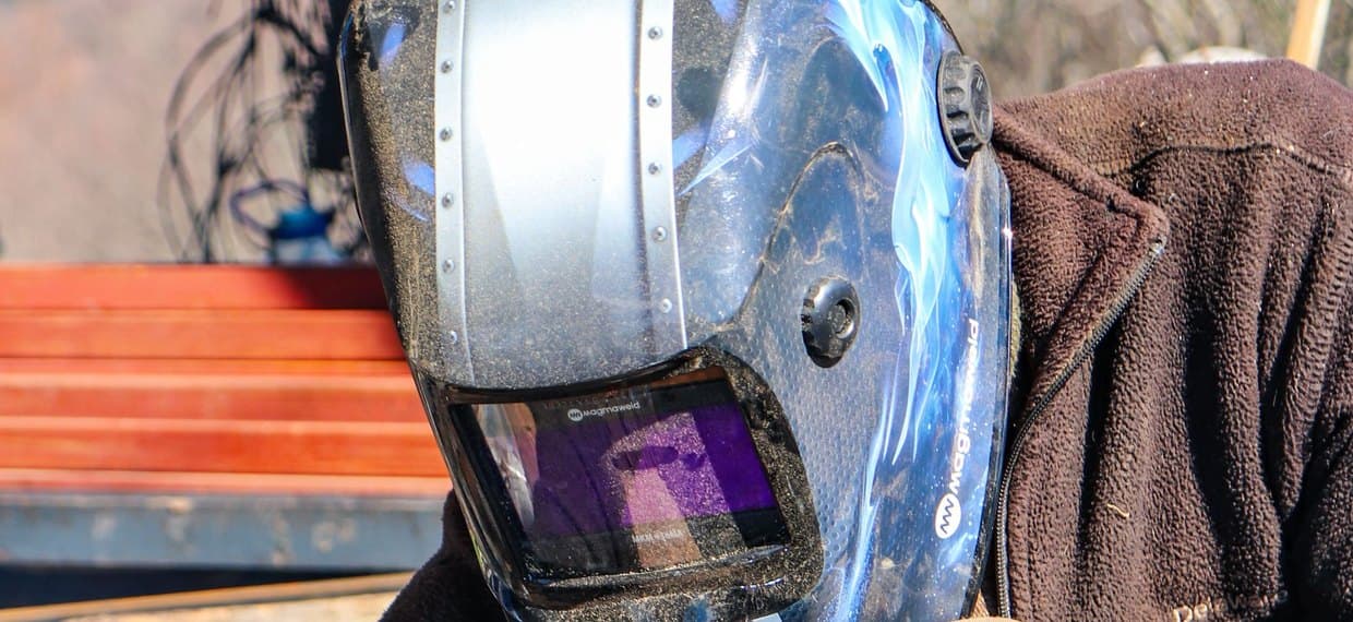 A welder's auto-darkening helmet seen close up, the dark filter window and the shade control knob on the side of the shell