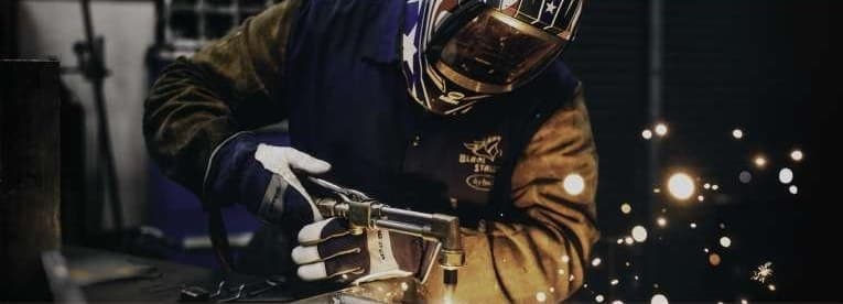 A welder in a hood joining two steel plates, sparks flying from the arc