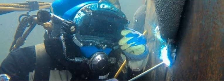 A diver in a blue helmet welding a rusted steel surface underwater