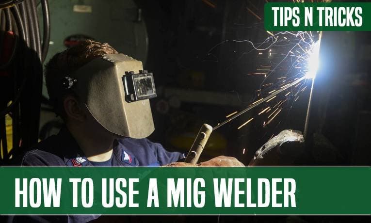 A welder in a hood laying a MIG bead, sparks arcing from the joint