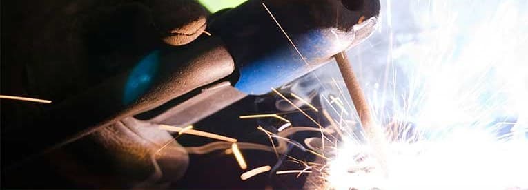 A close-up of gloved hands holding a torch, sparks streaming from the arc