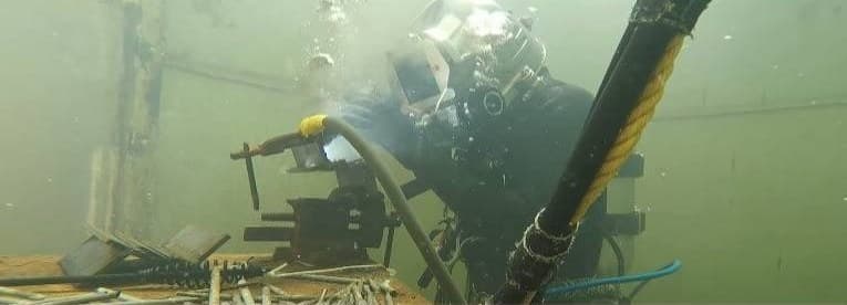 A diver in a full-face mask welding underwater, umbilical hose over his shoulder