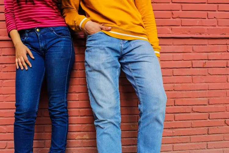 Two people standing against a brick wall in ordinary blue jeans