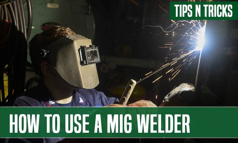 A welder in a hood laying a MIG bead, sparks arcing from the joint