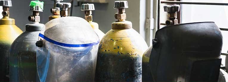 A row of welding gas cylinders standing against a workshop wall