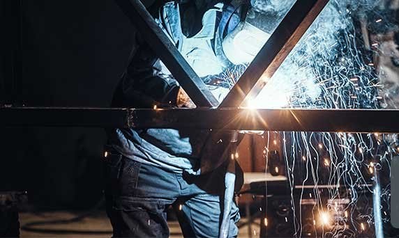 A welder cutting into a steel frame, sparks falling past his legs