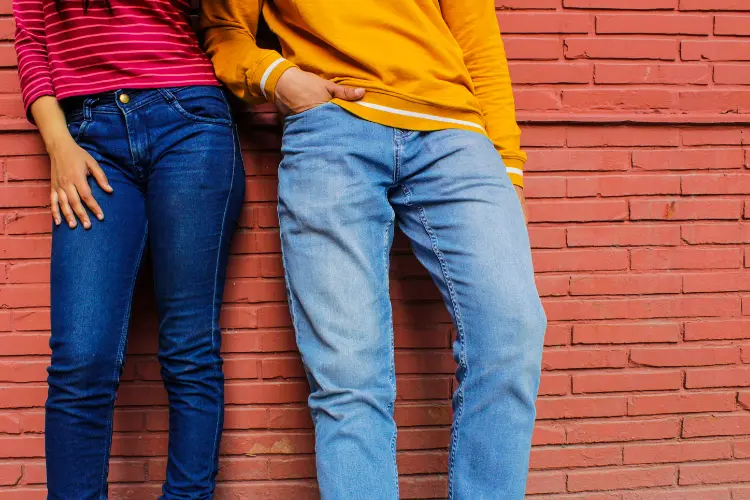 Two people standing against a brick wall in ordinary blue jeans