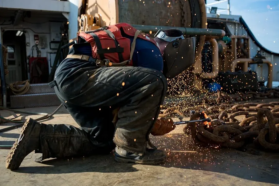 A welder crouching to cut steel, sparks bouncing off his trouser legs